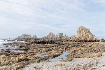 A serene, rocky beach with various jagged formations and scattered pools of water under a partly cloudy sky