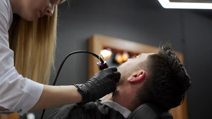Professional barber gives stylish haircut to male client in modern salon. Expert hairdresser uses clippers, scissors for trendy mens hairstyle. Grooming session, haircutting with precision.