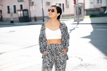 Young beautiful smiling hipster woman in trendy summer zebra print costume clothes. Carefree model posing in the street at sunset. Positive brunette female. Cheerful and happy. In sunglasses