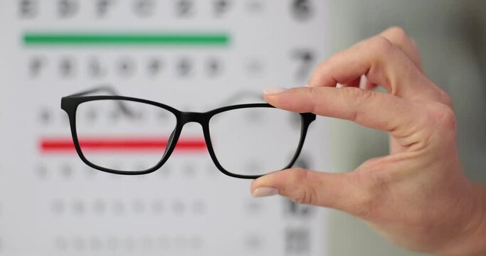 Person confidently holds glasses in front of eye test chart