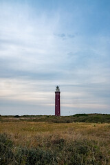 This image presents a solitary red lighthouse rising above a sprawling heathland along the coast. The lighthouse's stark, vertical lines contrast with the horizontal expanse of the natural landscape