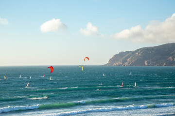 View of the Atlantic Ocean with surfers and windsurfers in the water against of the blue sky and...