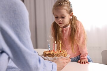 Birthday celebration. Mother holding tasty cake with burning candles near her daughter indoors