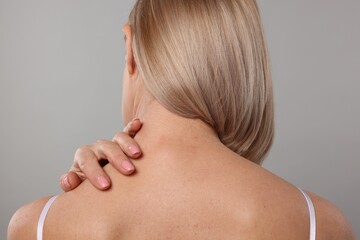 Woman suffering from pain in her neck on grey background, back view