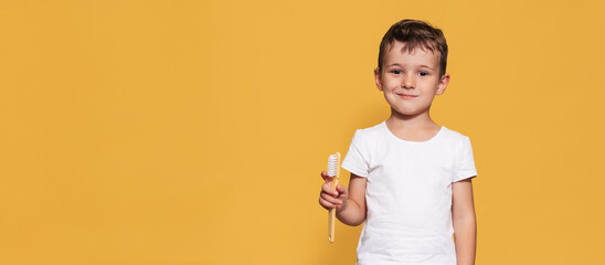 A smiling boy with healthy teeth holds a plus tooth and a toothbrush on a isolated background. Oral hygiene. Pediatric dentistry. Prevention of caries. A place for your text.