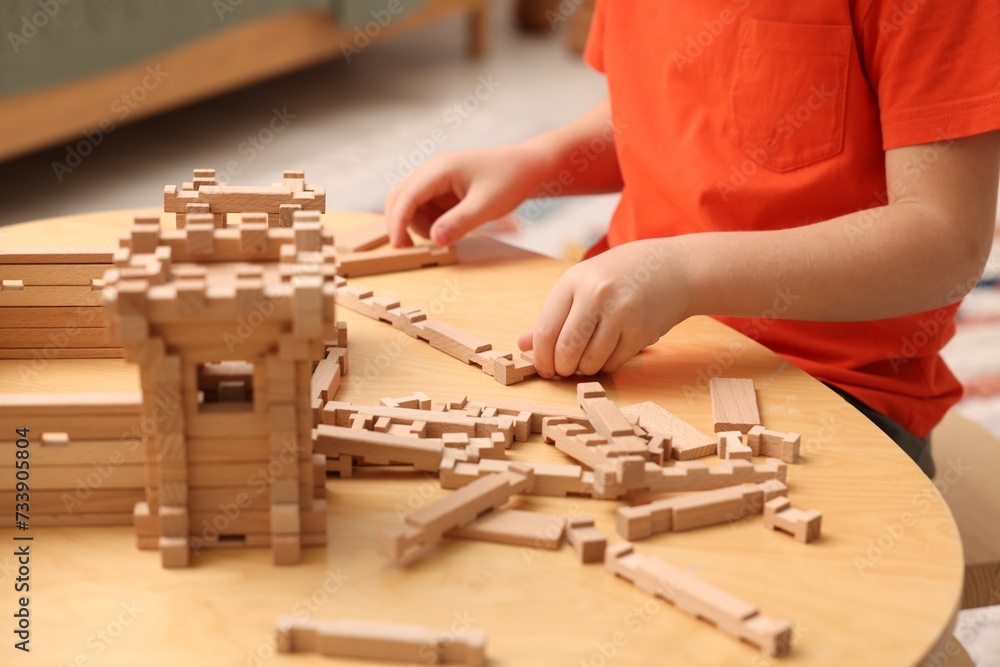 Sticker Little boy playing with wooden construction set at table in room, closeup. Child's toy