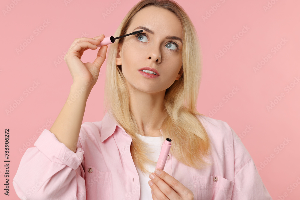 Wall mural Beautiful woman applying mascara on pink background