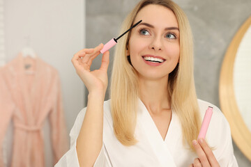 Beautiful happy woman applying mascara in bathroom