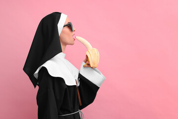 Woman in nun habit with banana against pink background, space for text. Sexy costume