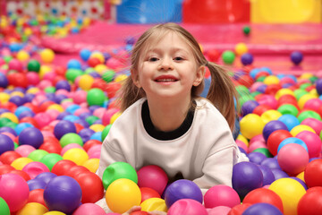 Fototapeta na wymiar Happy little girl lying on colorful balls in ball pit