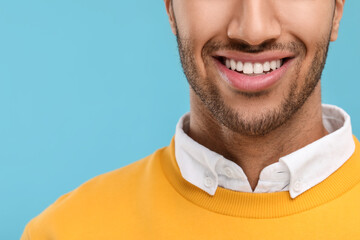 Smiling man with healthy clean teeth on light blue background, closeup. Space for text