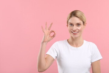 Woman with clean teeth smiling and showing OK gesture on pink background, space for text