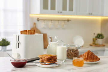Fototapeta na wymiar Making toasts for breakfast. Appliance, crunchy bread, honey, jam, milk and croissant on white marble table in kitchen