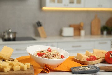 Delicious pasta with grated cheese and tomatoes on white table in kitchen