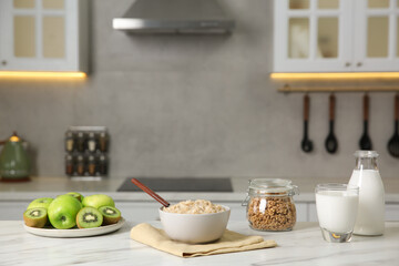 Breakfast time. Tasty oatmeal in bowl, fruits, granola and milk on white marble table