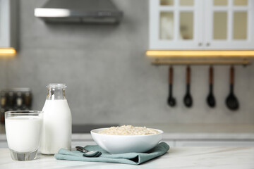 Breakfast time. Tasty oatmeal in bowl and milk on white marble table. Space for text