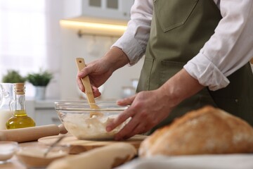Obraz na płótnie Canvas Making bread. Man preparing dough in bowl at wooden table in kitchen, closeup