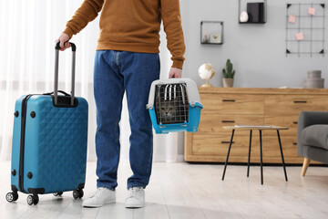 Travel with pet. Man holding carrier with cute cat and suitcase at home, closeup. Space for text - obrazy, fototapety, plakaty