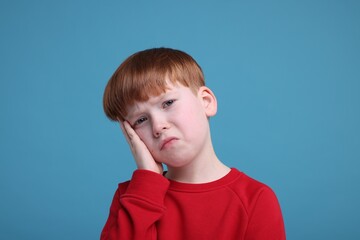 Portrait of sad little boy on light blue background