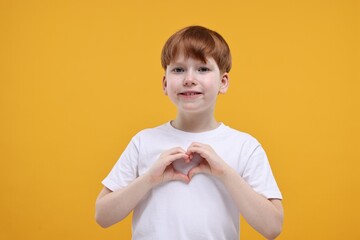 Cute little boy showing heart gesture with hands on orange background