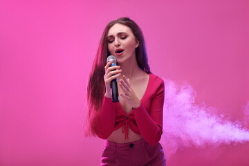 Emotional woman with microphone singing on pink background