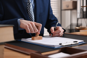 Notary with pen stamping document at table in office, closeup