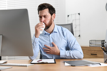 Sick man with tissue coughing at workplace in office - obrazy, fototapety, plakaty
