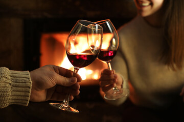 Couple clinking glasses of wine near fireplace at home, closeup
