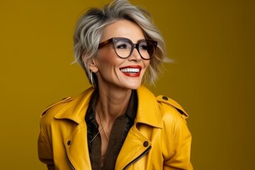 Portrait of young happy smiling woman in yellow jacket and glasses, over yellow background