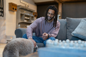 Man with dreads sitting on sofa and petting dog