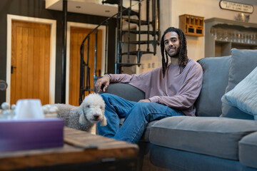 Man with dreads relaxing on sofa with dog on side