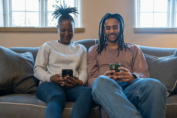 Happy couple using phone while sitting on sofa in cozy living room