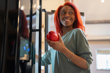 Woman holding bell pepper next to open fridge 