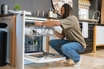 Man with dreads crouching next to open dishwasher