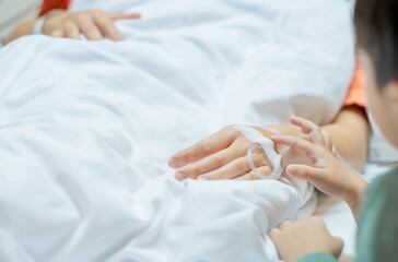 Woman lying in the hospital bed sleeping, Hand of her son holds it comfortingly. Soft focus. Copy space.
