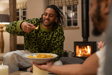 Smiling friends relaxing at home, sharing tortilla chips