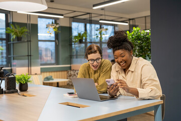 Smiling businesswomen using phone and laptop in office