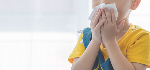 Little boy blowing nose into tissue paper and wearing surgical face mask. Copy space.
