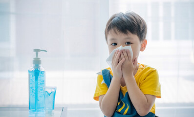 Little boy blowing nose into tissue paper and wearing surgical face mask. Copy space.