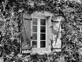 Black and white photo of traditional French farmhouse window with old shabby shutters 
