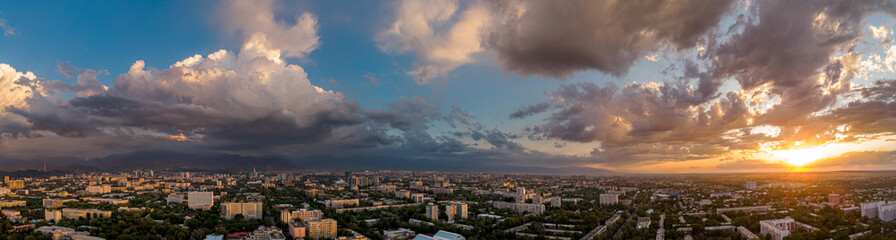Panorama of a beautiful orange sunset against the backdrop of the city landscape. Large cumulus clouds. Almaty city. Kazakhstan