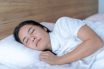 Calm Asian woman sleeping and sweet dreams lying on a comfortable bed in a cozy bedroom in the morning feeling relaxed..Way of life, relaxation, good health, and simple living. Health care concept.
