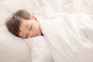 Fototapeta na wymiar Adorable little boy sleeping in white bed. people, children, rest and comfort concept. Soft focus. Copy space.