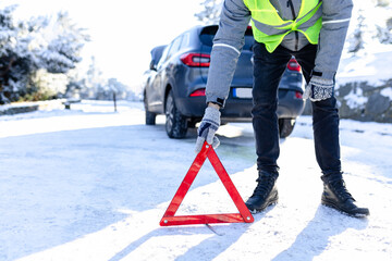 Car breakdown concept. Man driver placing warning triangle on snowy road.
