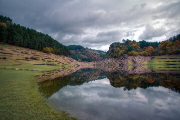 Naklejka premium The canyoning of the Mino river near Portomarin is reflected in the calm waters of the river