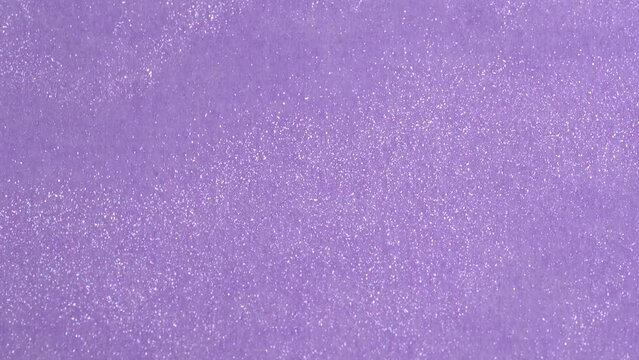 Shimmering vivid silver liquid glowing particles flow motion on lavender paper background. Shiny liquid lotion texture on light purple background. Glowing particles.