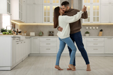 Fototapeta na wymiar Affectionate young couple dancing and kissing in kitchen. Space for text