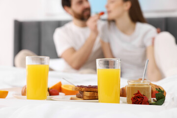 Tray with tasty breakfast on bed. Husband feeding his wife in bedroom, selective focus