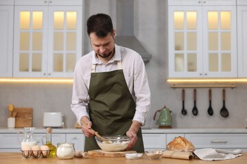 Making bread. Man preparing dough in bowl at wooden table in kitchen