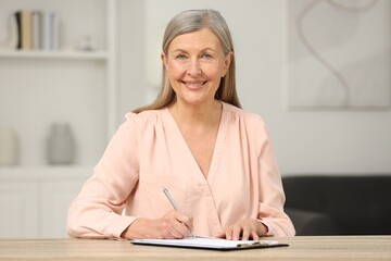 Smiling senior woman signing Last Will and Testament at wooden table indoors